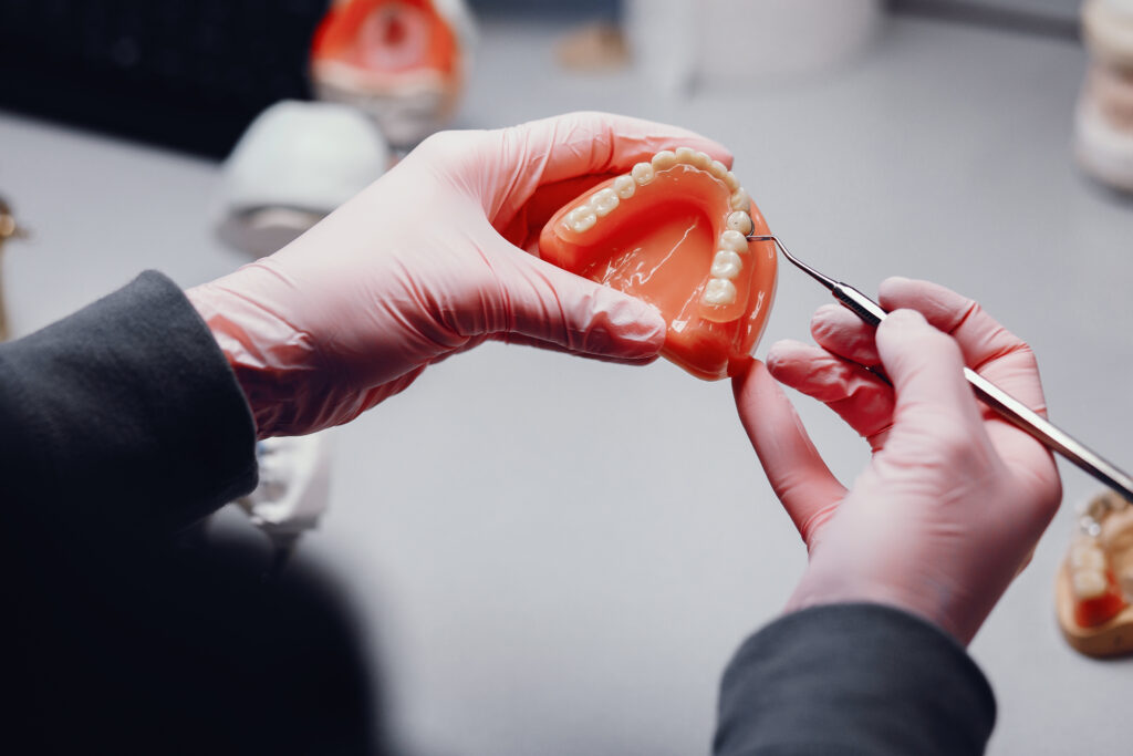 Zbliżenie na dłonie protetyka w różowych rękawiczkach trzymającego i oglądającego model protezy dentystycznej, ilustrujące szczegółową pracę protetyki stomatologicznej na warszawskim Ursynowie.